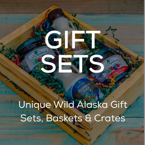 White text stating "Gift Sets: Unique Wild Alaska Gift Sets, Baskets & Crates" on top of an image of an alaska gift set with fruit syrup, birch syrup and wild berry jams.