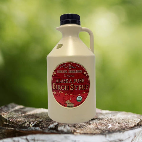 Kahiltna Birchworks Alaska Pure Birch Syrup, 32 oz white plastic jug displayed on a birch log outdoors