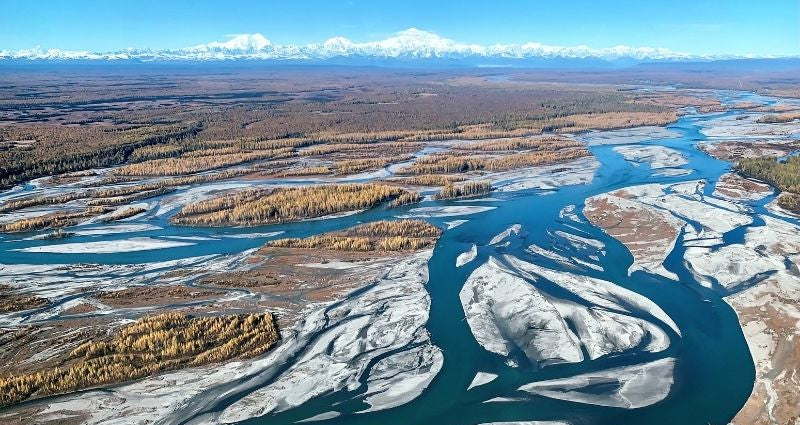 Alaska river system with ice and snow in a vast landscape under a clear blue sky.