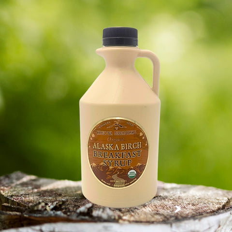 Kahiltna Birchworks Alaska Breakfast Syrup, 32 fl oz plastic jug made with Alaska Pure Birch Syrup, resting on a birch log