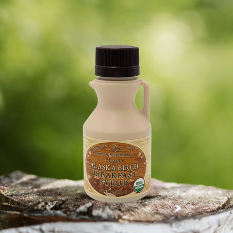 Kahiltna Birchworks Alaska Breakfast Syrup, 3.4 fl oz plastic jug made with Alaska Pure Birch Syrup, resting on a birch log