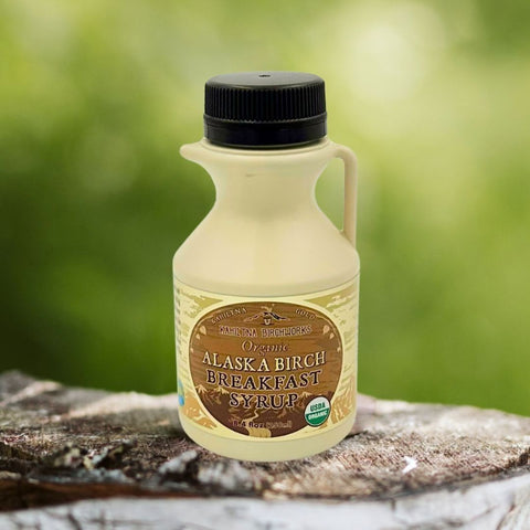 Kahiltna Birchworks Alaska Breakfast Syrup, 8.4 fl oz plastic jug made with Alaska Pure Birch Syrup, resting on a birch log