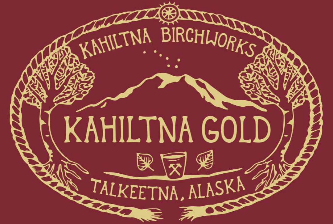 A graphic design featuring a cream-colored oval emblem with the text 'KAHILTNA BIRCHWORKS', 'KAHILTNA GOLD', and 'TALKEETNA, ALASKA' surrounding mountain and tree illustrations, set against a solid dark red background.