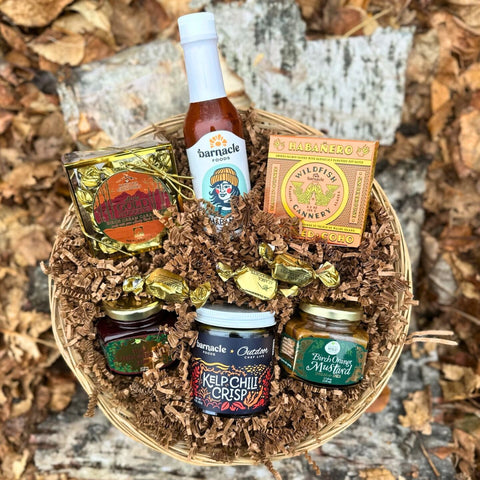 The Susitna Sweet and Spicy Gift Basket with various items including a bottle of hot sauce, jam, and jars on a wooden surface.