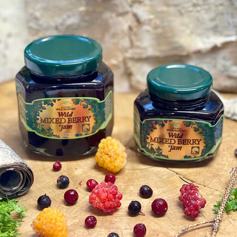 Two jars of Wild Mixed Berry Jam with fresh berries on a wooden surface.