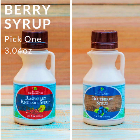 Two bottles of berry syrup with labels for raspberry rhubarb and blueberry on a wooden surface.