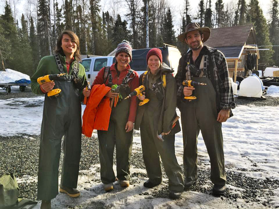 Four people in winter clothing holding drills for tapping birch trees