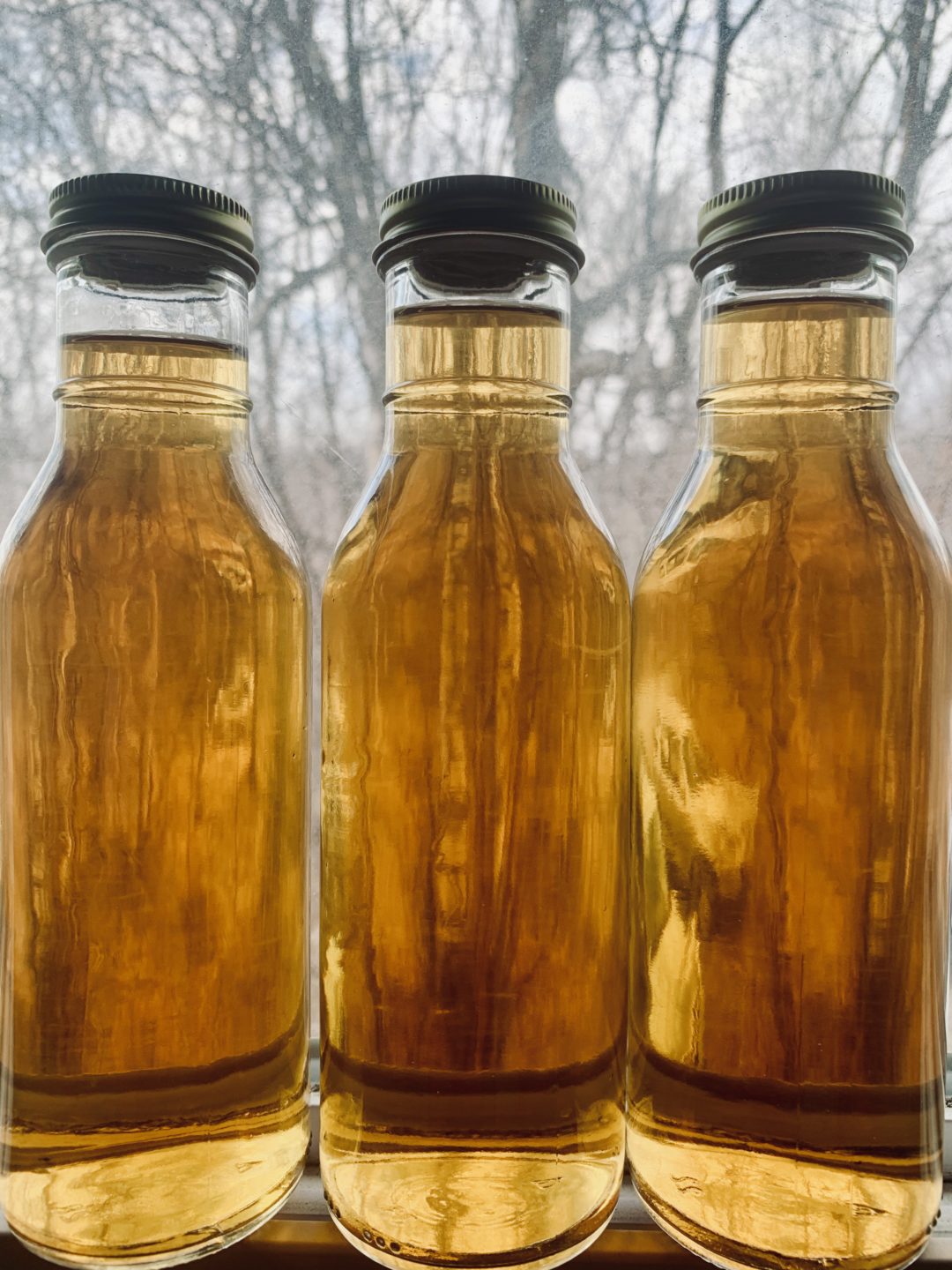 Three bottles of birch water with black caps against a blurred natural background