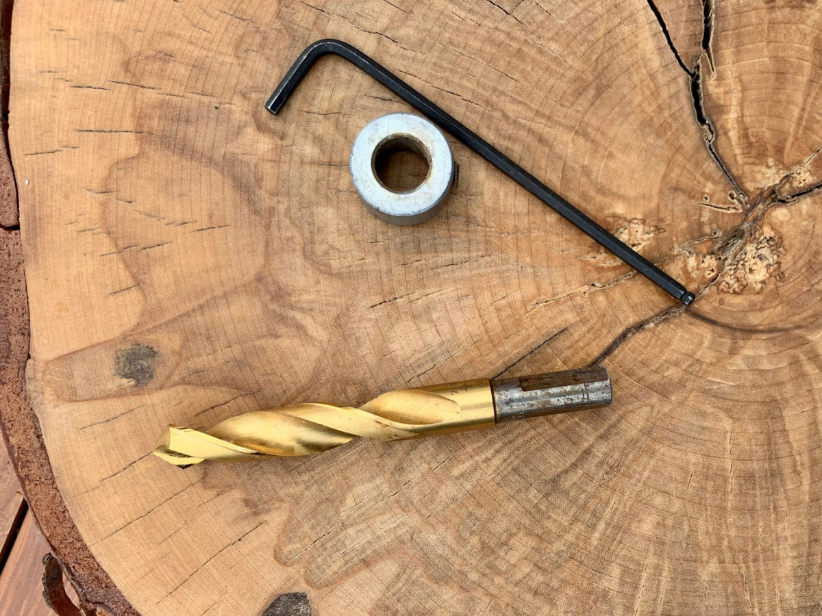 Gold drill bit, black hex key, and metal washer on a wooden surface