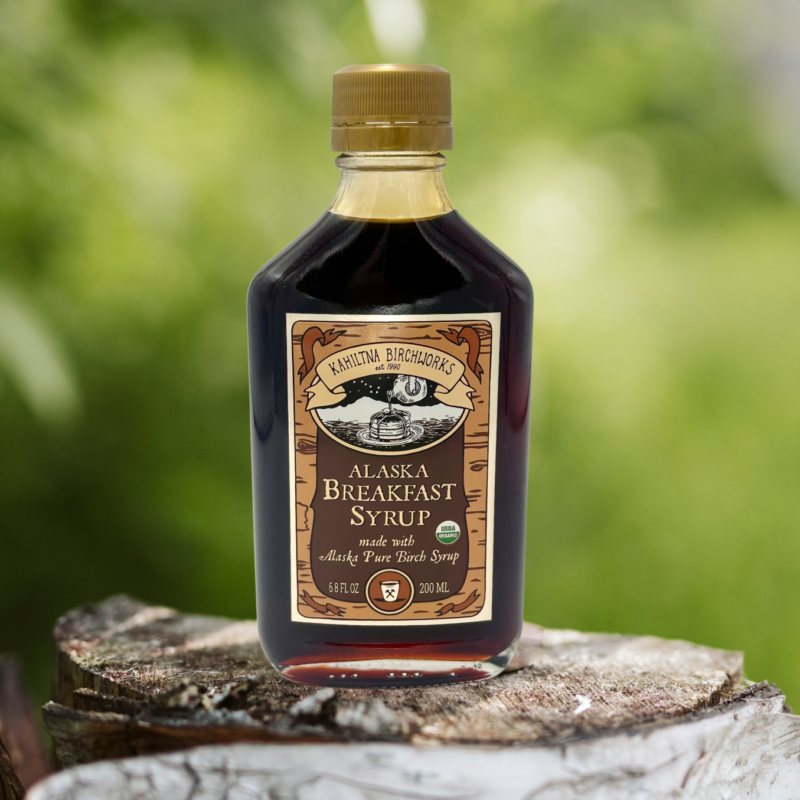 Kahiltna Birchworks Alaska Breakfast Syrup, 6.8 fl oz bottle made with Alaska Pure Birch Syrup, resting on a birch log