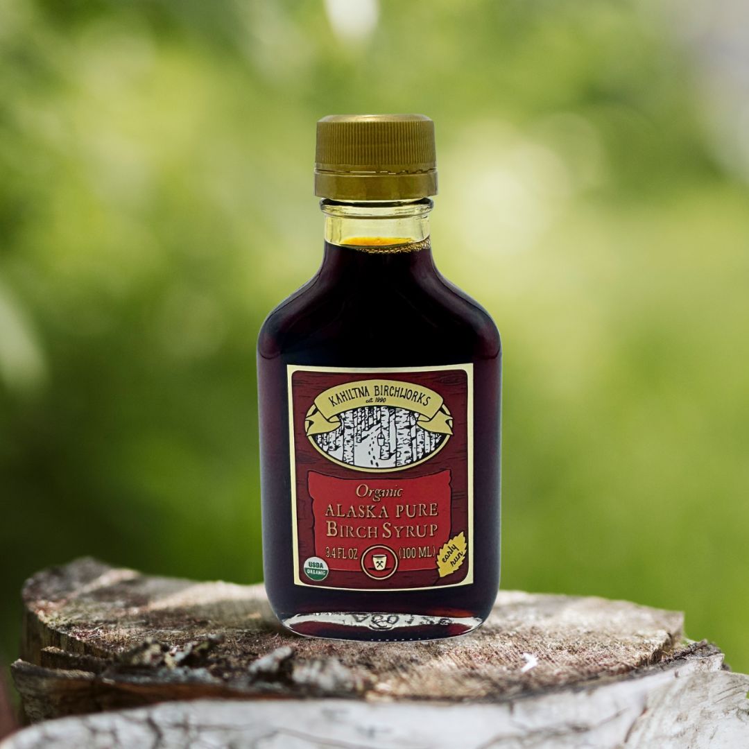 Kahiltna Birchworks Organic Alaska Pure Birch Syrup, 3.4 fl oz early run bottle resting on a birch log