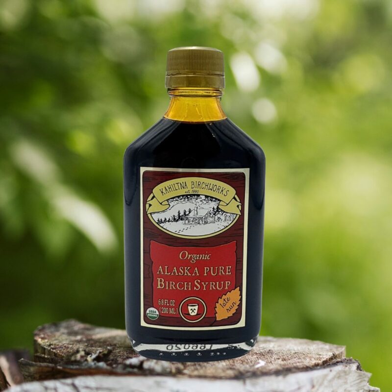 Kahiltna Birchworks Organic Alaska Pure Birch Syrup, 6.8 fl oz late run bottle resting on a birch log